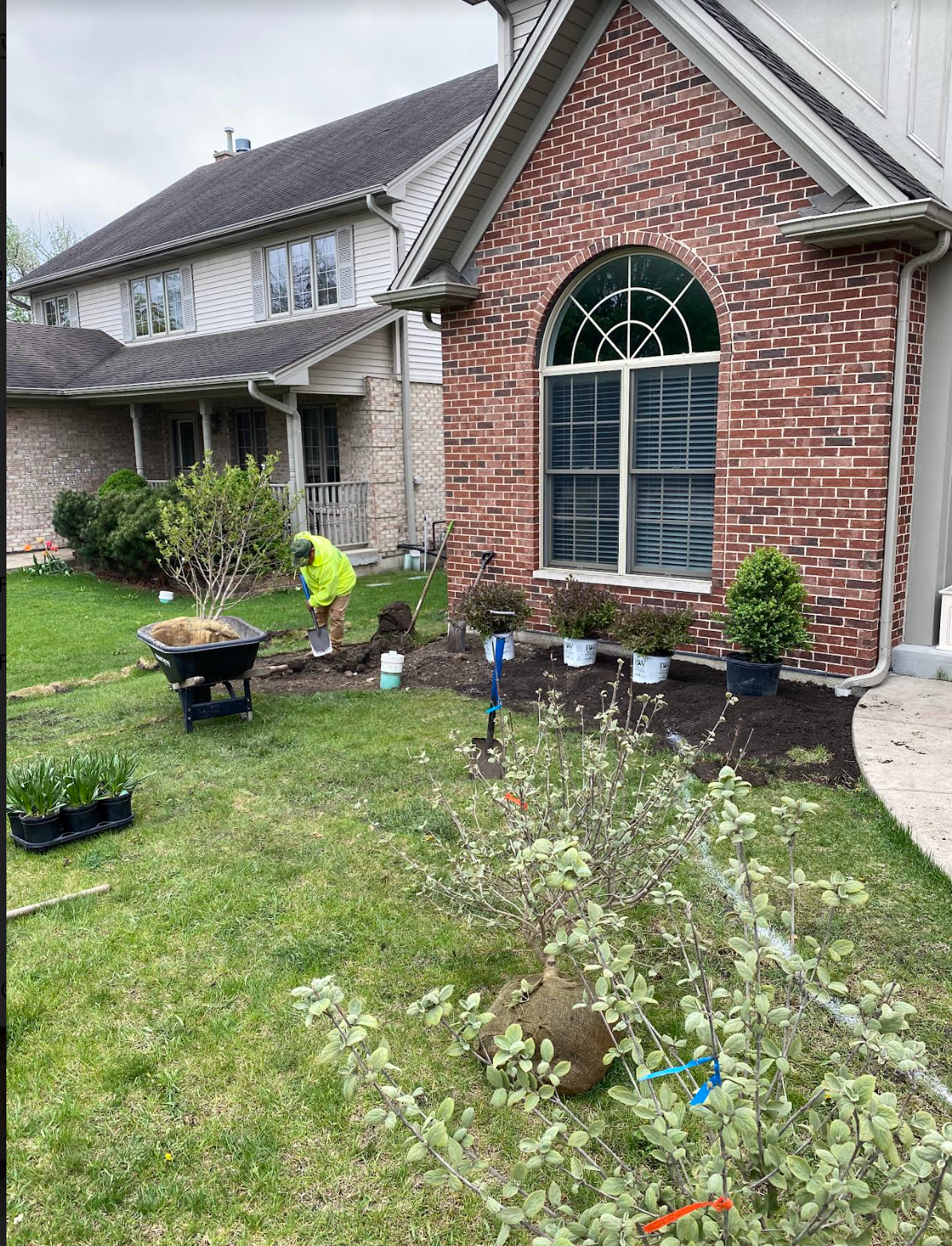 A man is planting a garden in front of a brick house.