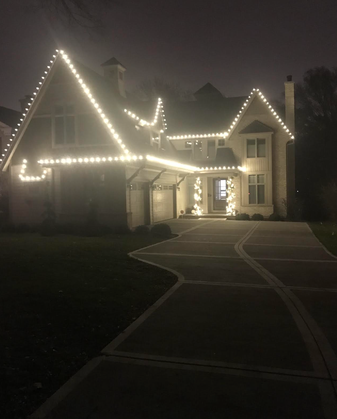 A house with christmas lights on the roof is lit up at night.