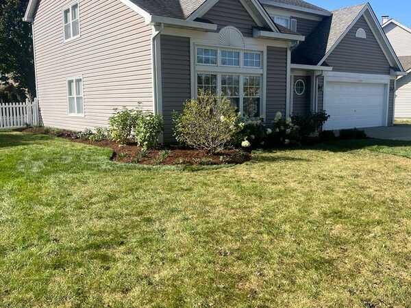 House exterior with beige siding, manicured lawn, and landscaping beds with mulch.