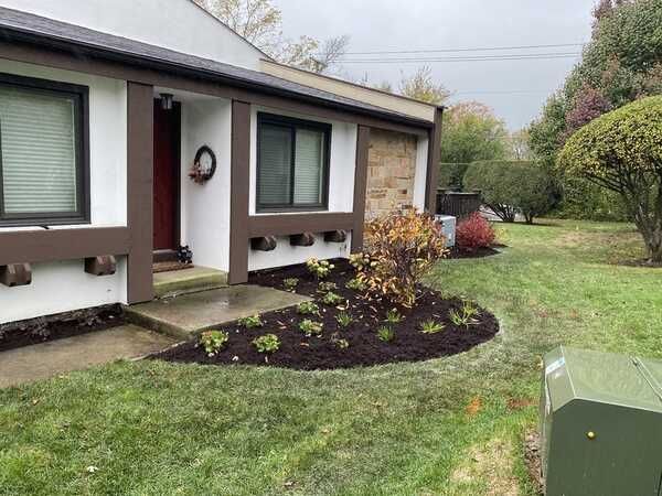 Exterior of a house with freshly mulched flowerbed, green lawn, brown trim, and overcast sky.