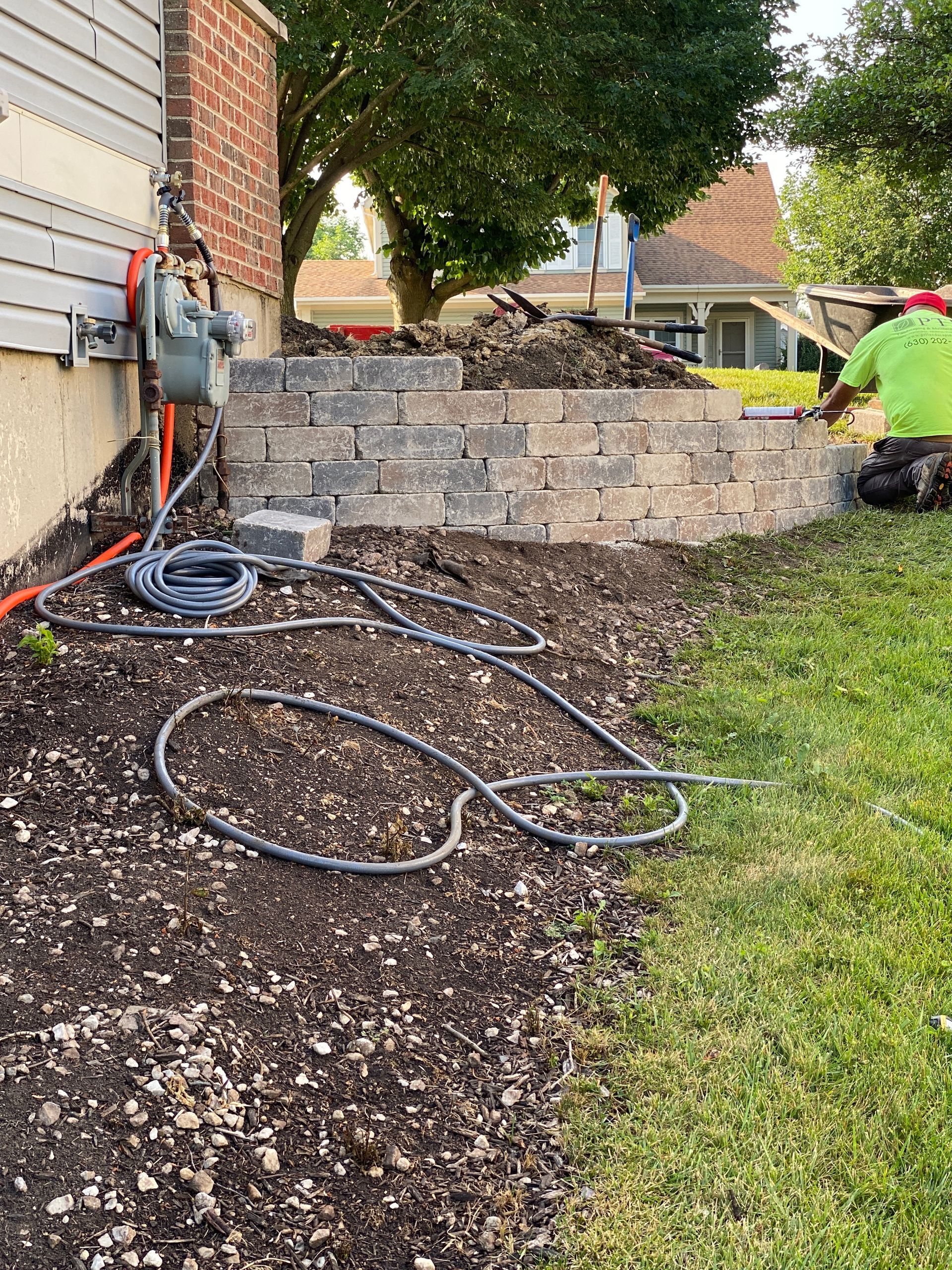 A man is kneeling in the grass next to a brick wall.