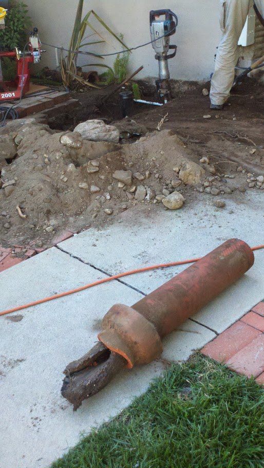 A large pipe is laying on the sidewalk next to a cord.