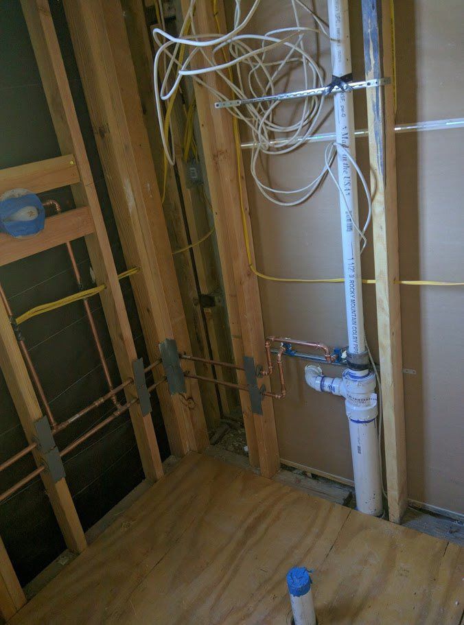 A bathroom under construction with pipes and wires hanging from the ceiling.