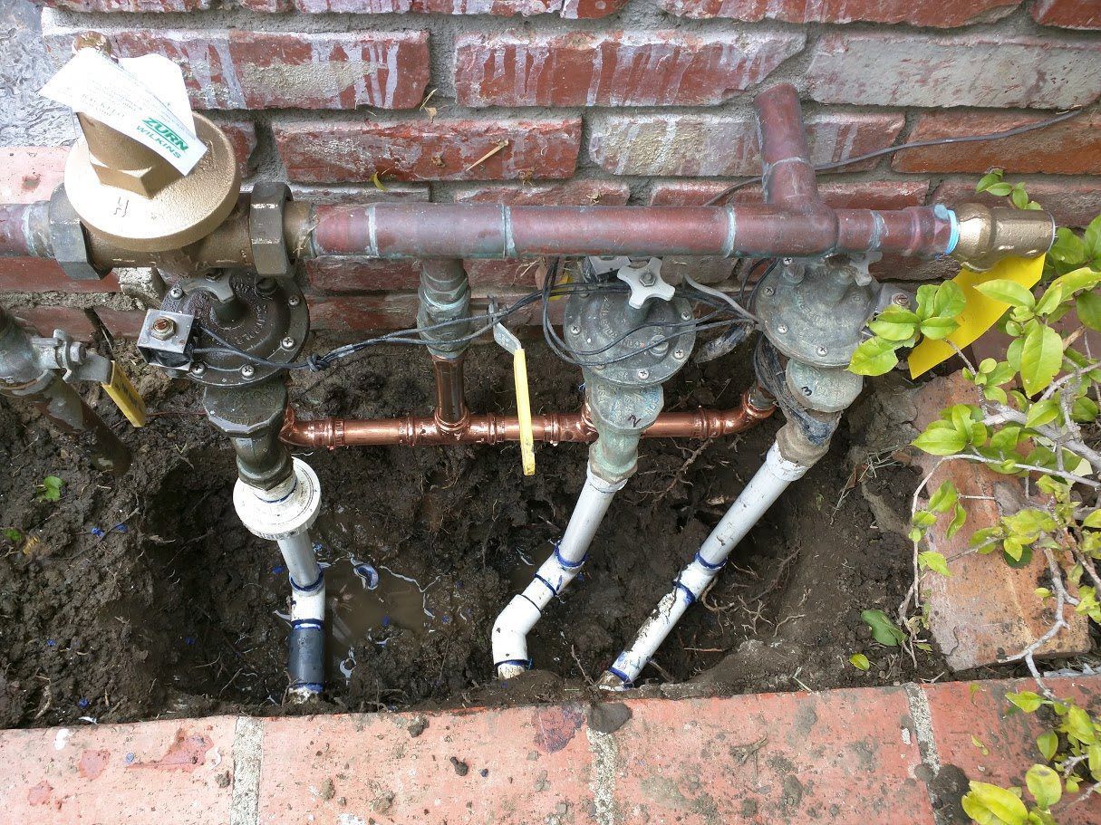 A bunch of pipes are sitting in the dirt next to a brick wall.