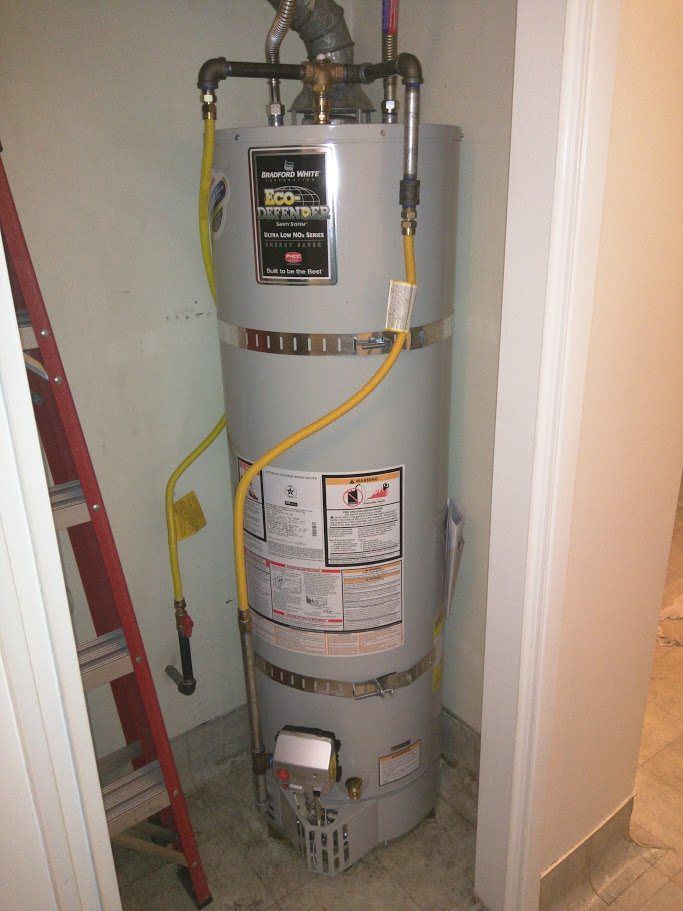 A water heater is sitting in a room next to a ladder.