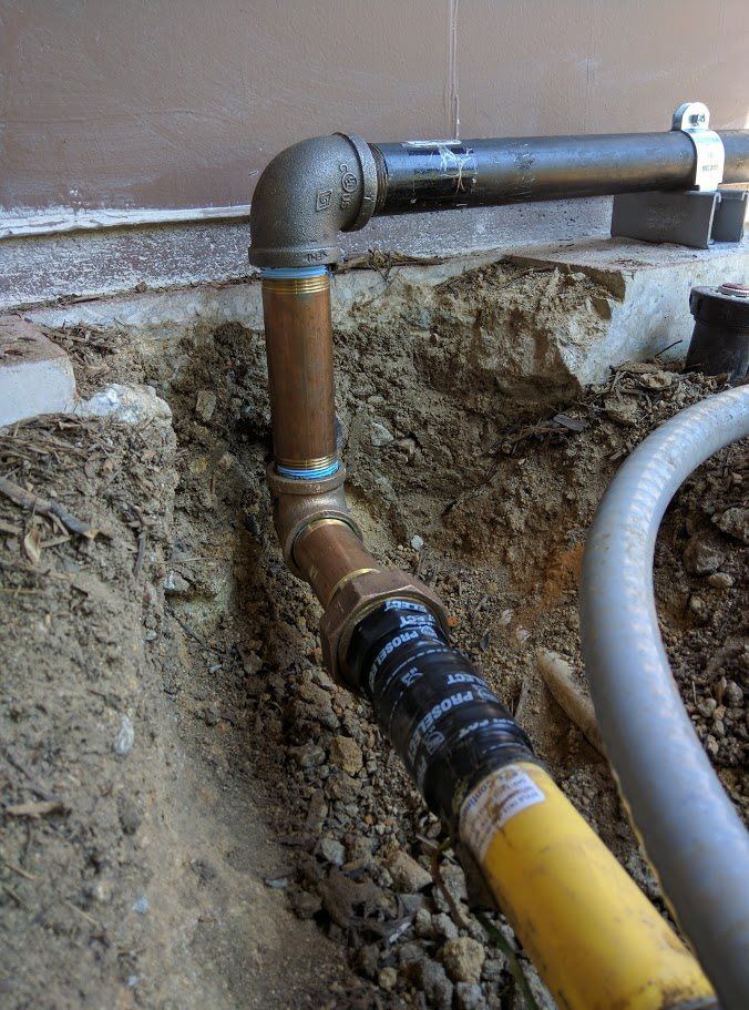 A pipe is being installed in the dirt next to a wall.