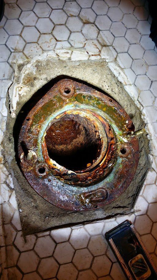 A rusty pipe is sitting on a tiled floor next to a level.
