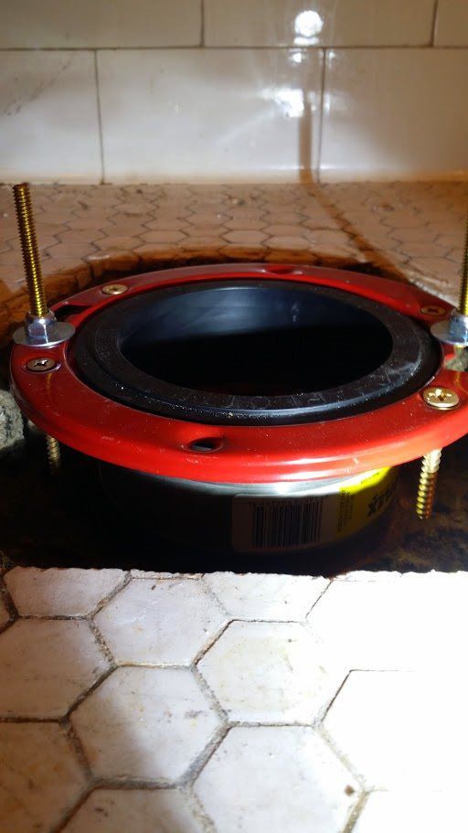A red toilet flange is sitting on top of a tiled floor.
