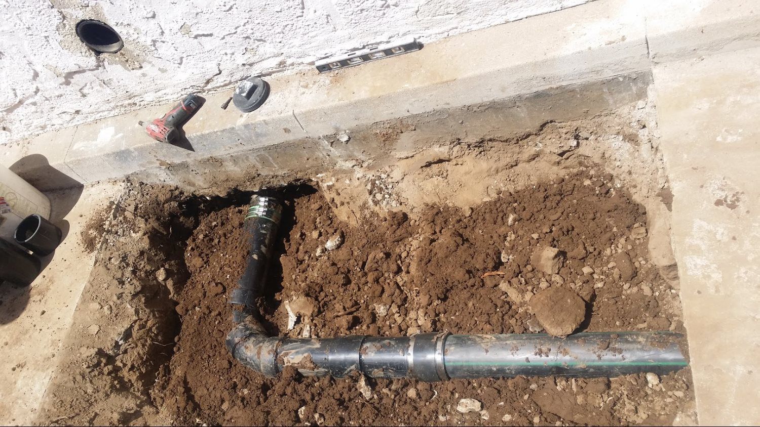 A pipe is laying in the dirt next to a wall.