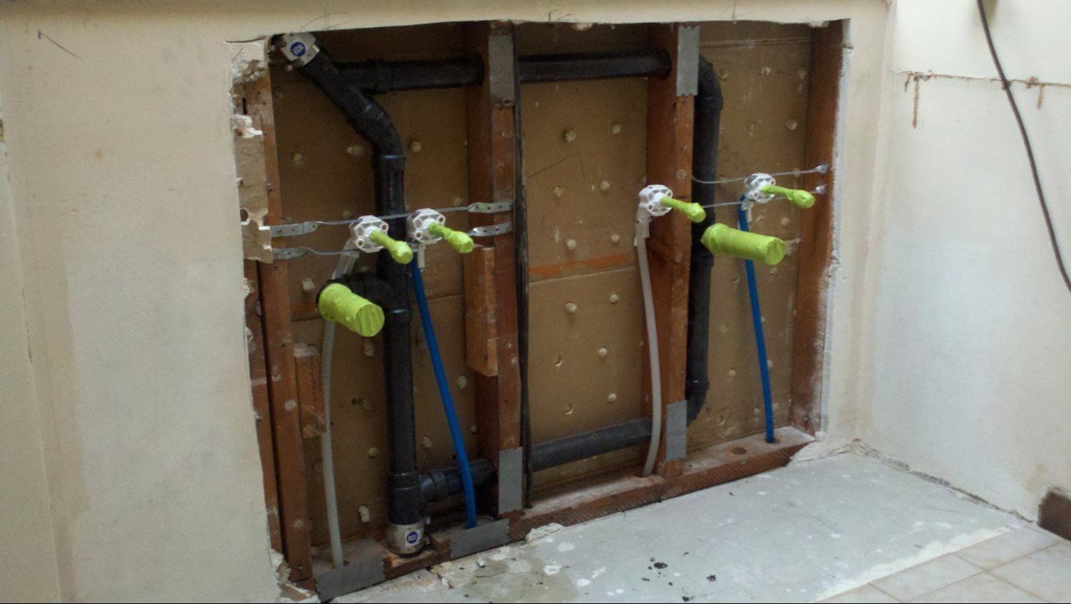 A bathroom with a hole in the wall and pipes coming out of it.