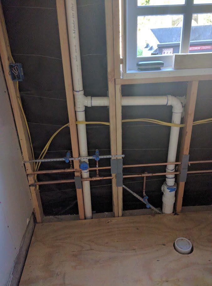 A bathroom under construction with pipes and wires coming out of the ceiling.