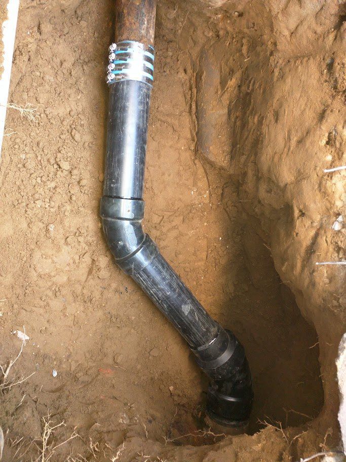 A black pipe is sitting in the dirt in a hole.