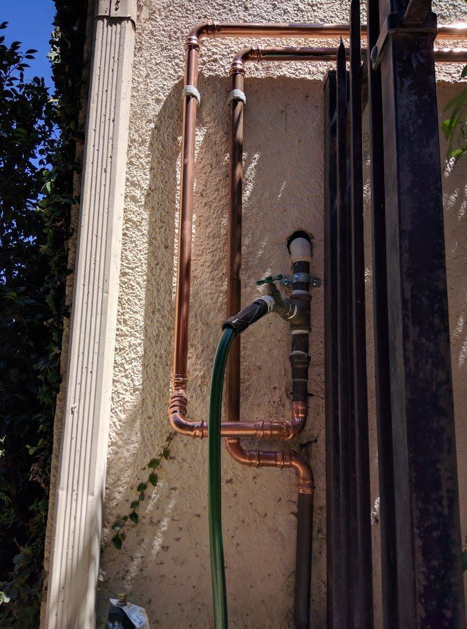 A hose is attached to a copper pipe on the side of a building