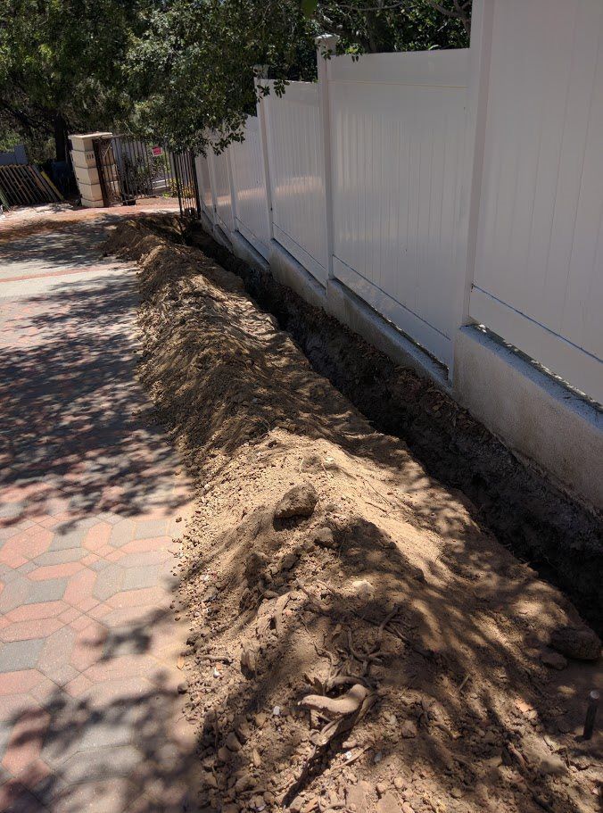 A pile of dirt is sitting next to a white fence.