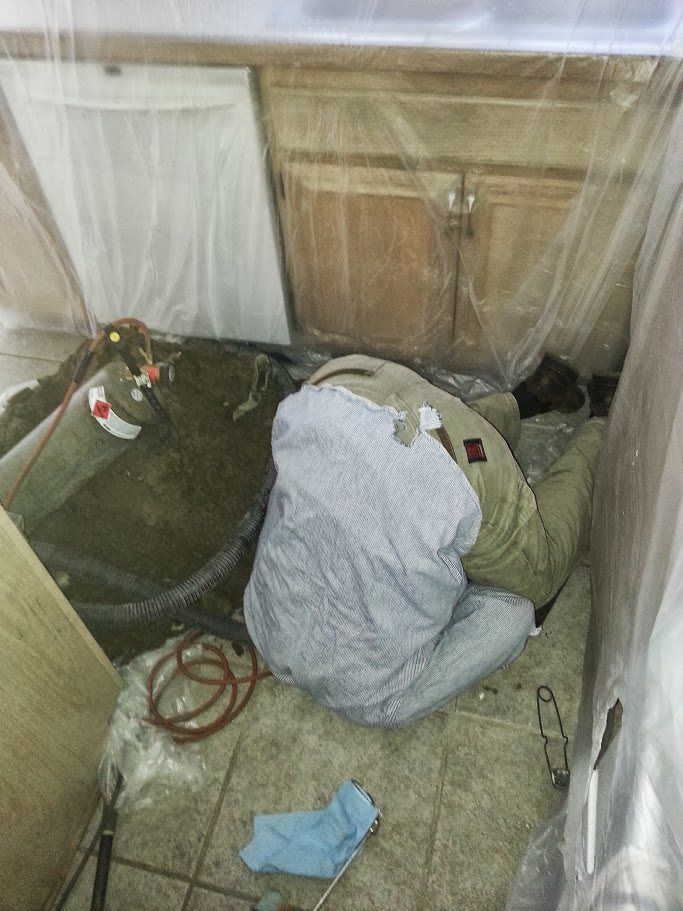 A man is laying on the floor in a kitchen under a sink.