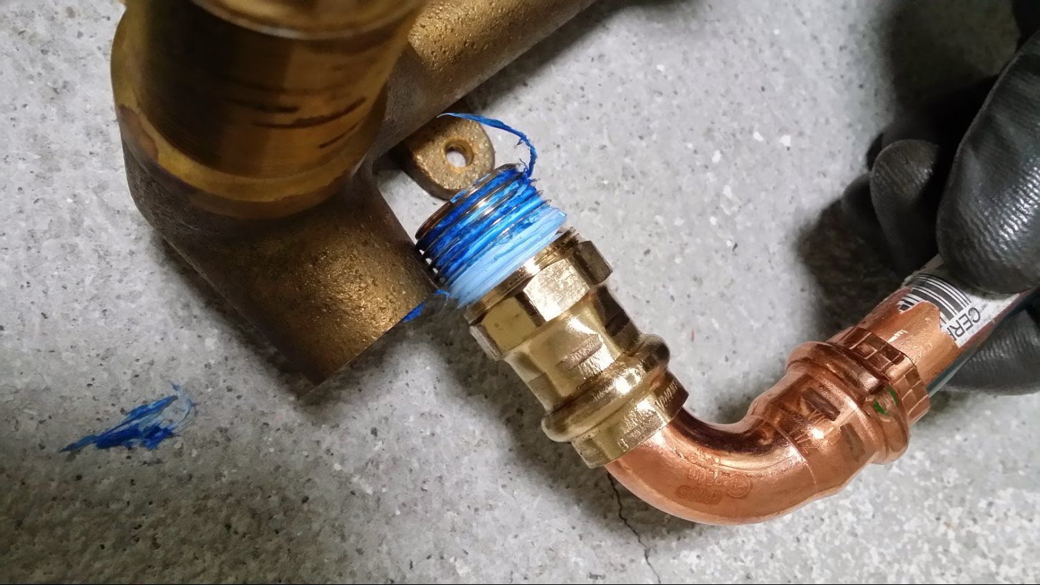 A person is holding a copper pipe with a blue string around it.