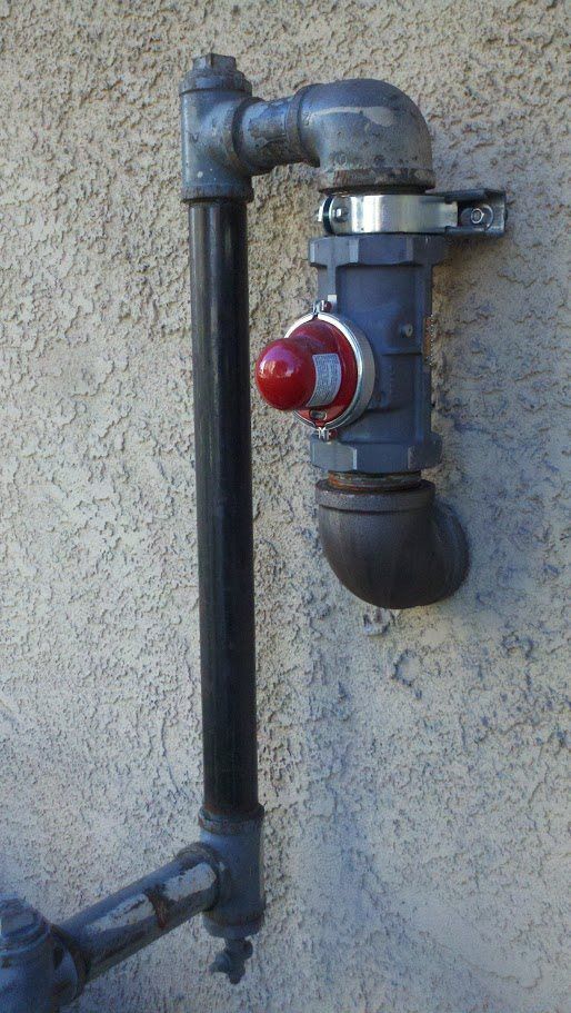 A pipe with a red button on it is attached to a wall.