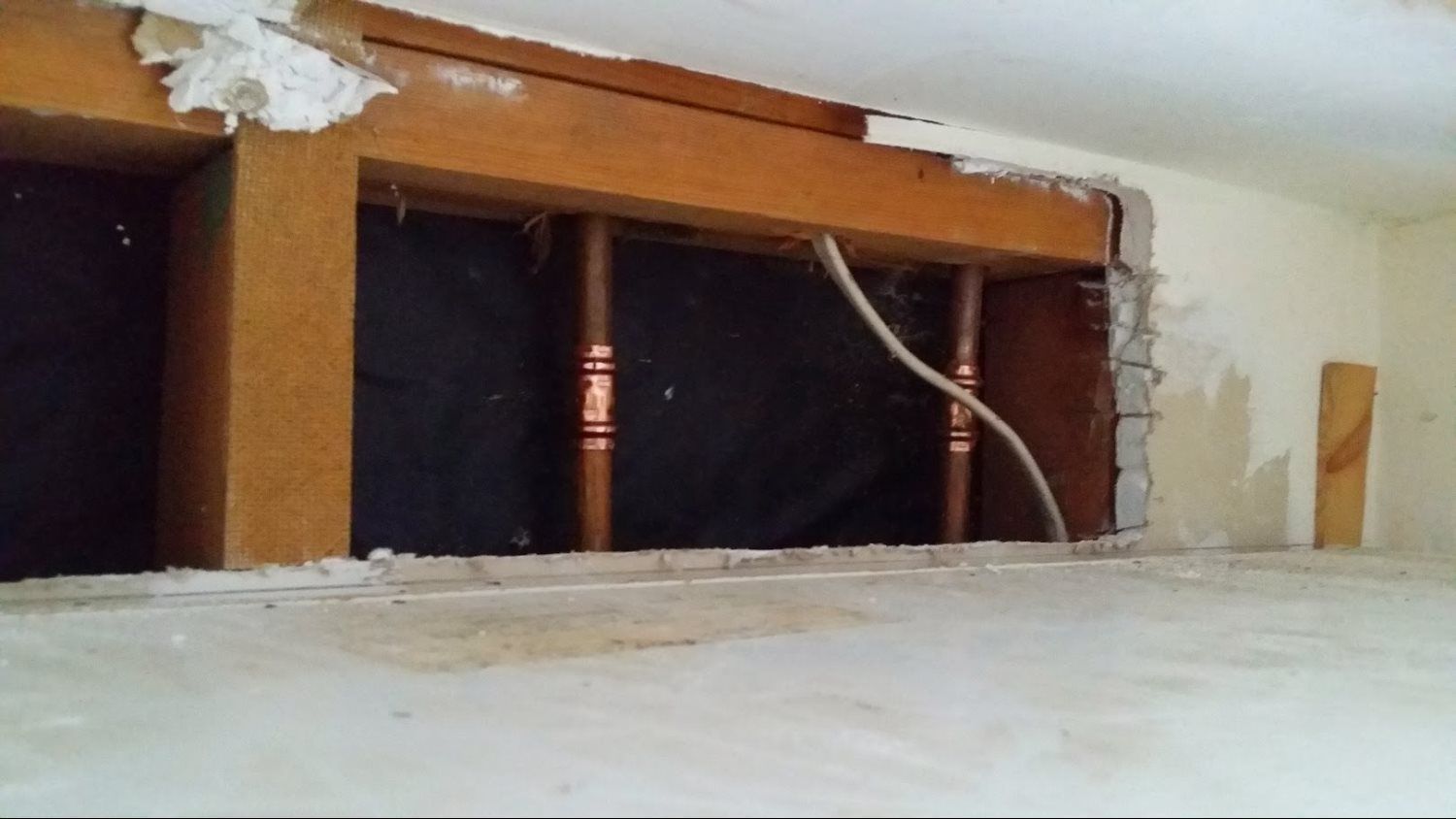 A hole in a wall with copper pipes coming out of it