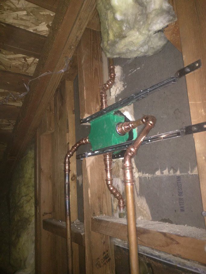 Copper pipes are connected to a green box in a wooden wall.
