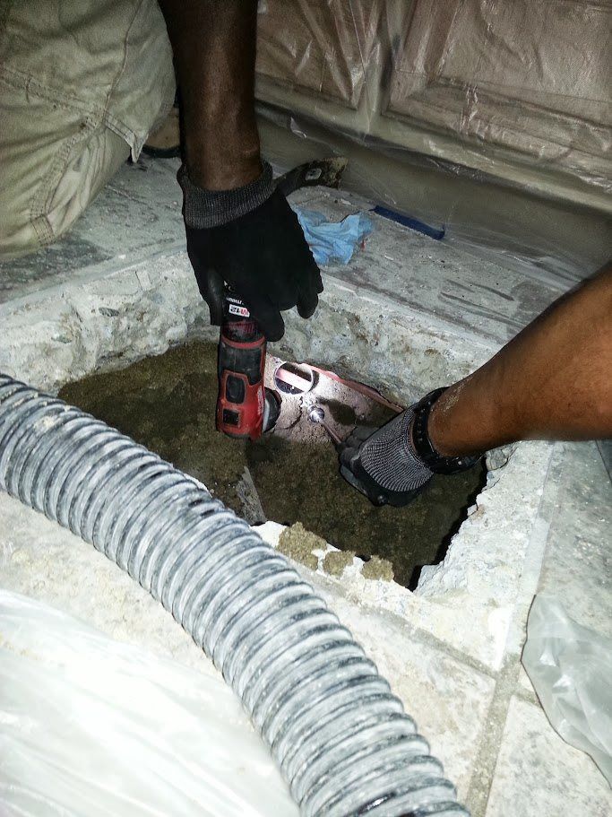 A person is using a vacuum hose to clean a hole in the floor.