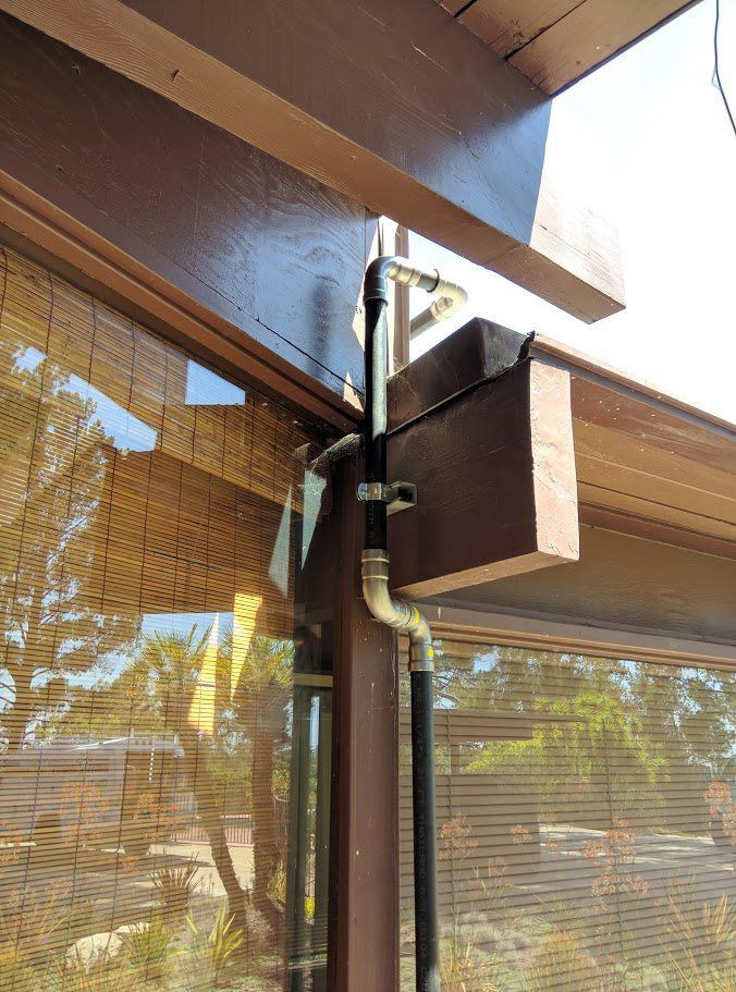 A pipe is attached to a wooden post next to a window.