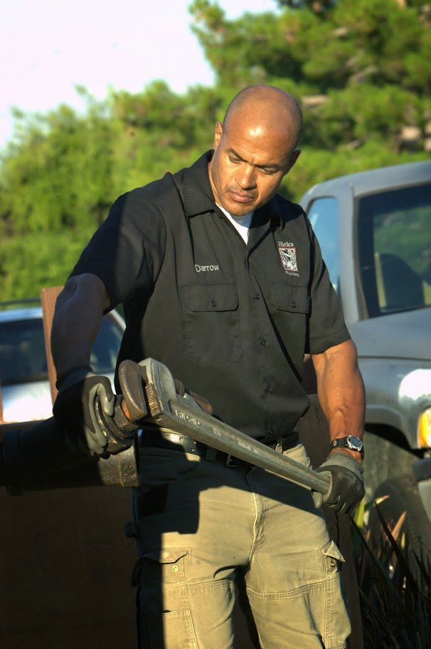 A man in a black shirt is holding a wrench in front of a truck.