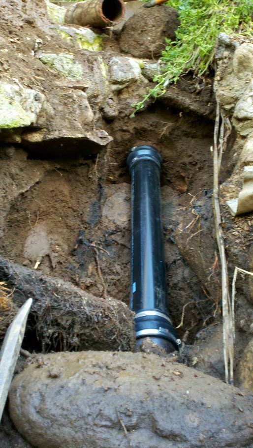 A black pipe is sitting in the dirt next to a rock.