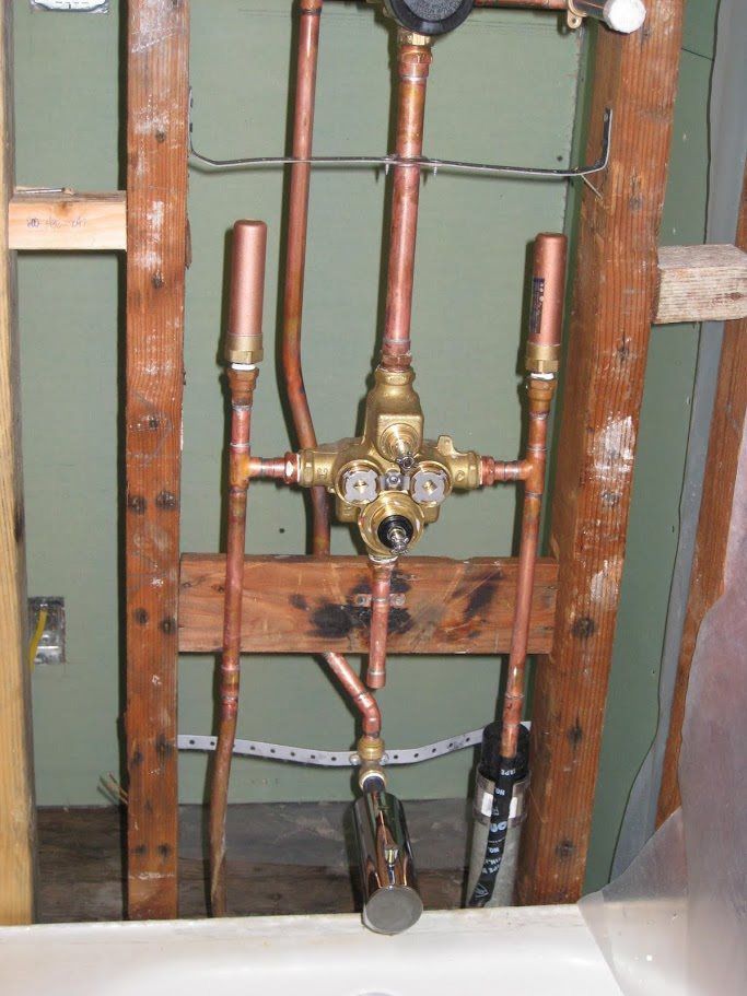 Copper pipes are hanging from a wooden frame in a bathroom