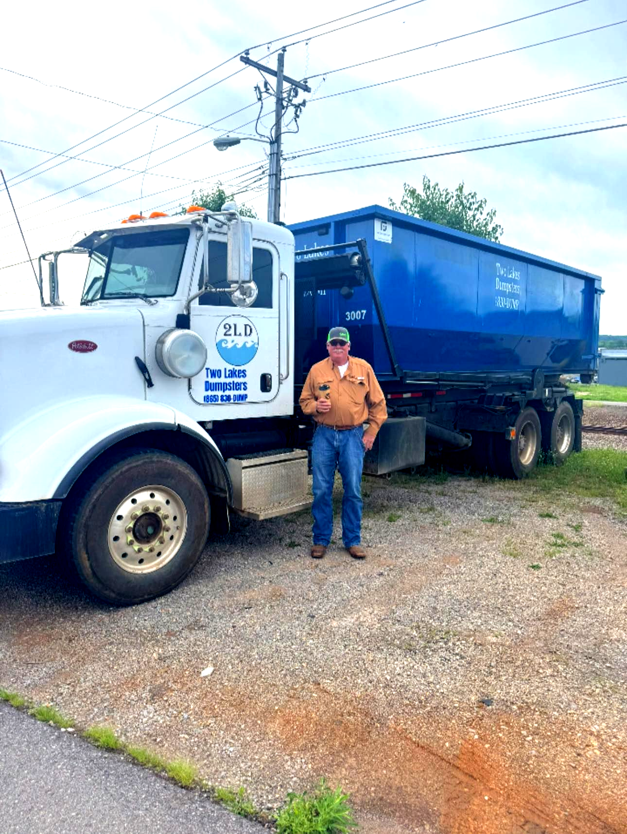 Blue dumpster on a trailer, filled with debris, parked on a driveway in front of a house.