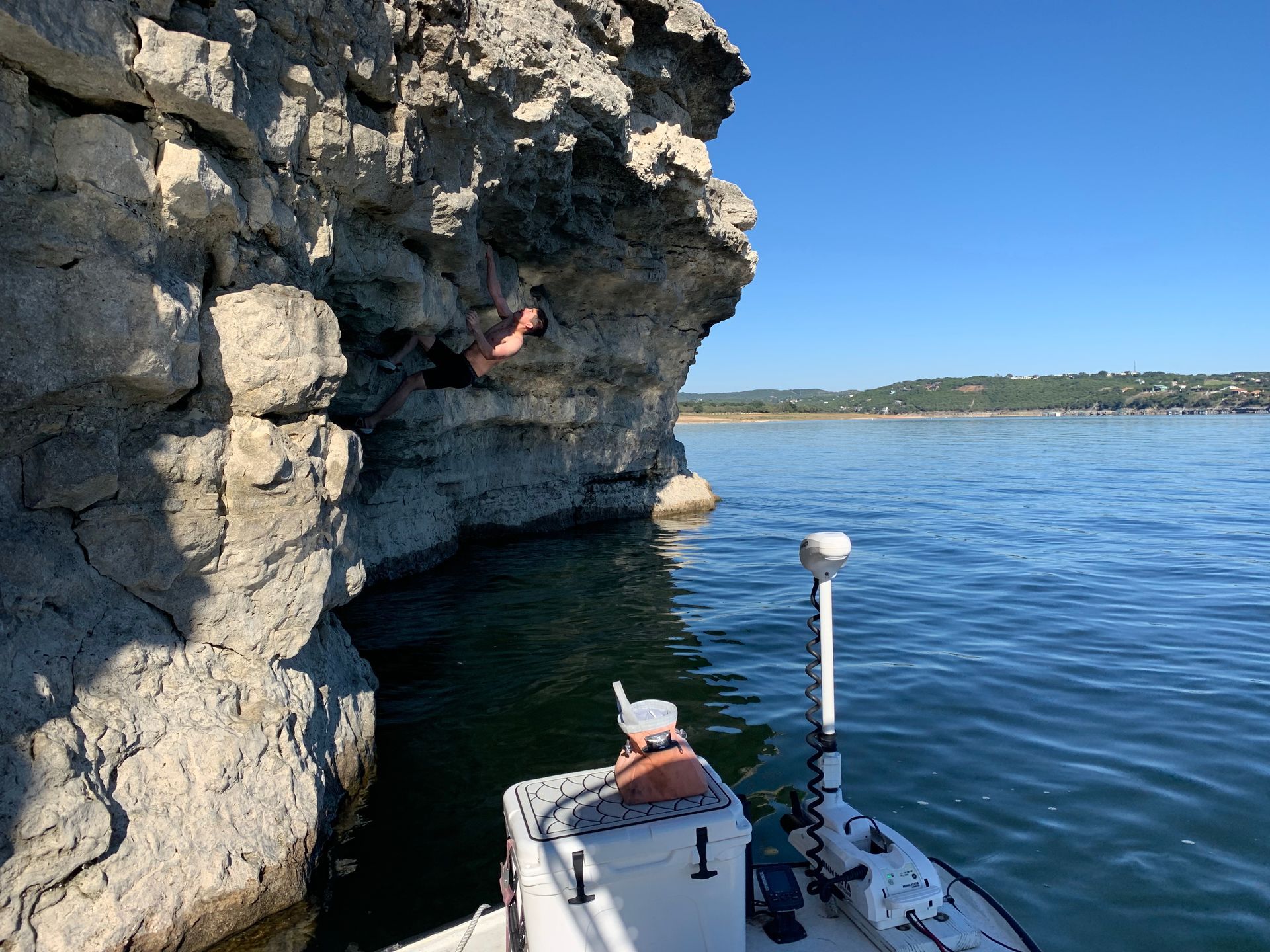 A person is climbing a rock wall next to a boat in the water.