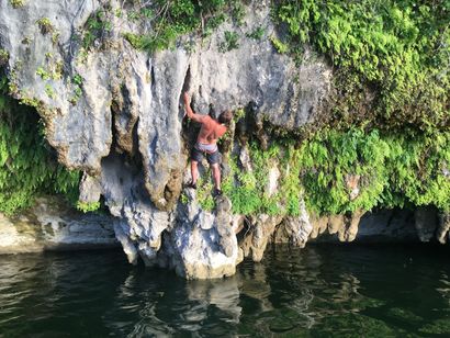 A man is climbing a rock overlooking a body of water.