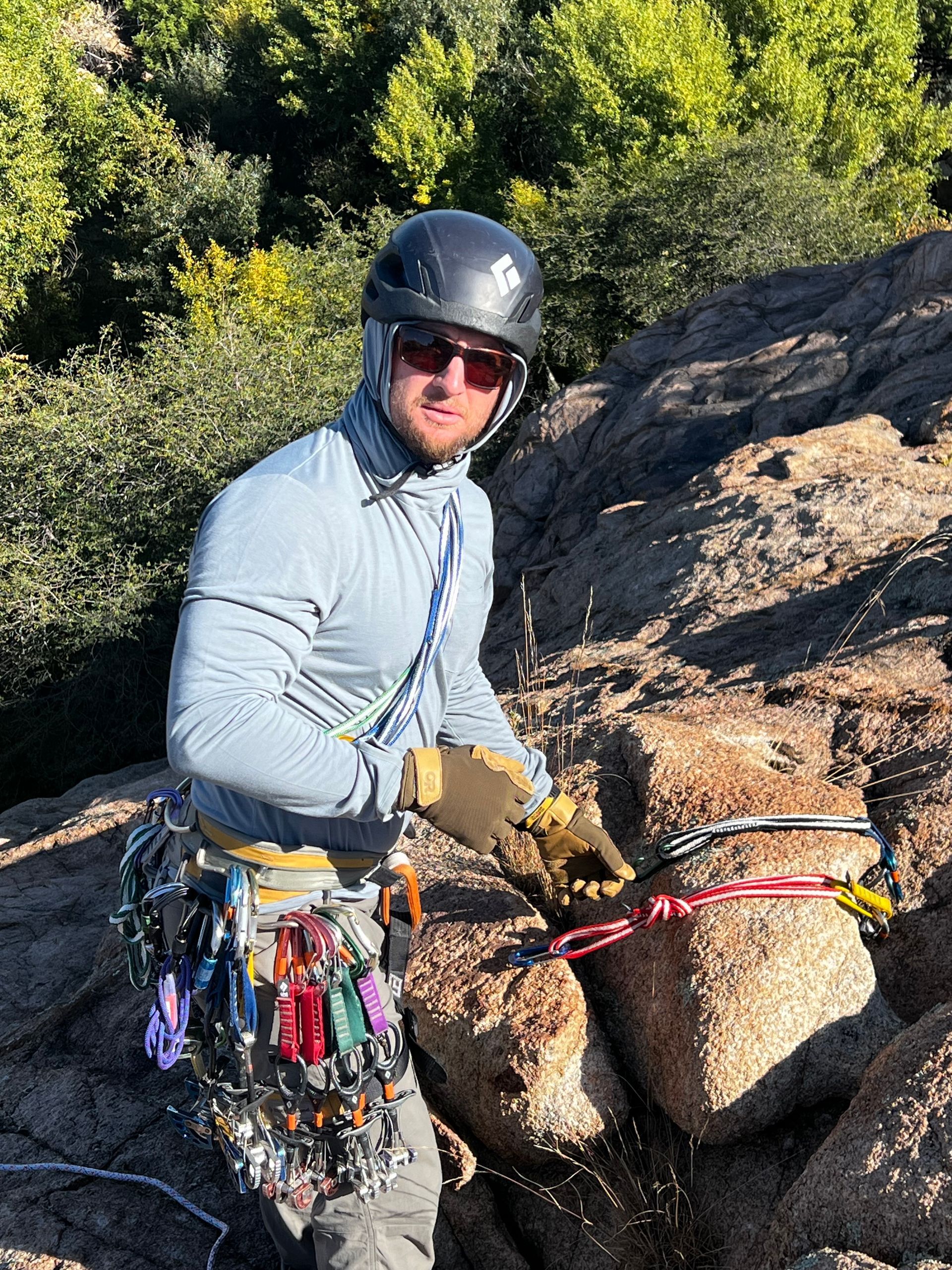 A man wearing a helmet and sunglasses is sitting on a rock.