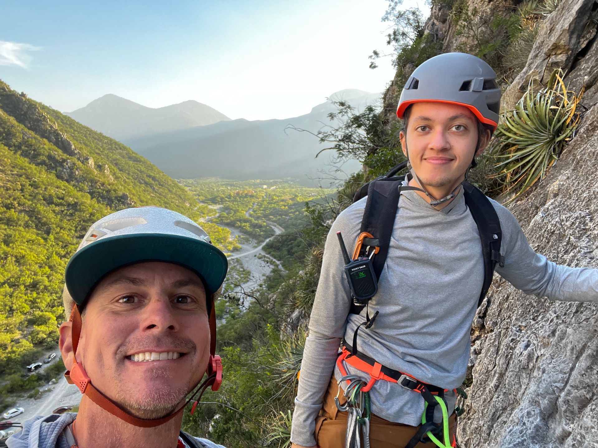 A man and a boy are standing next to each other on top of a mountain.