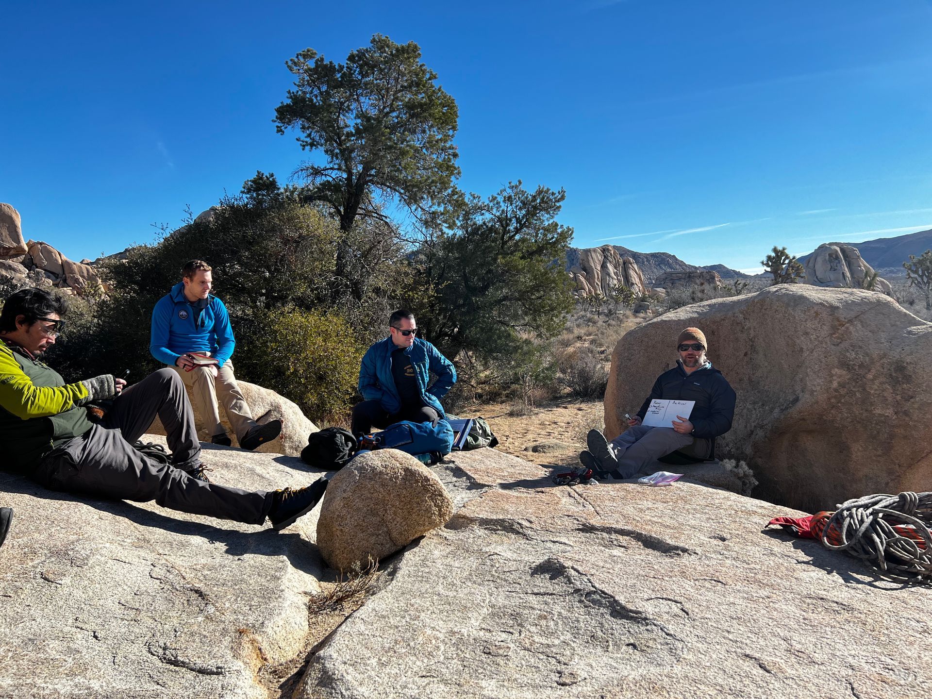 A group of people are sitting around a large rock.