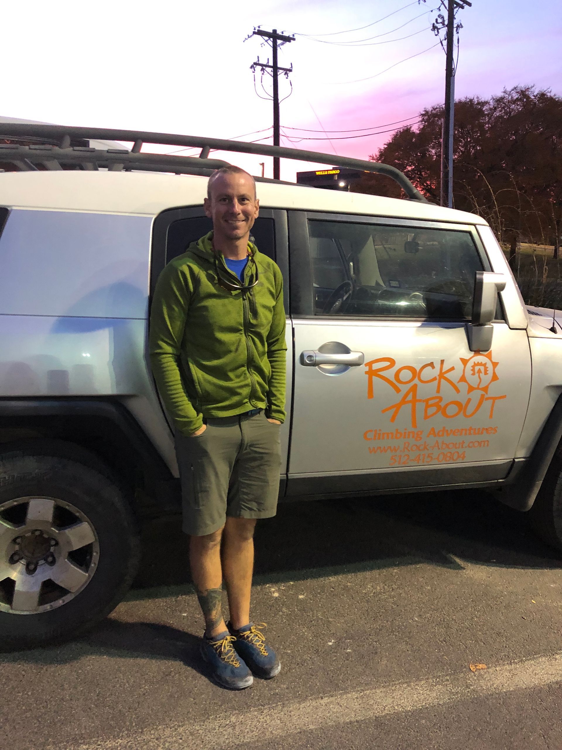 A man in a green jacket is standing in front of a jeep that says rock about