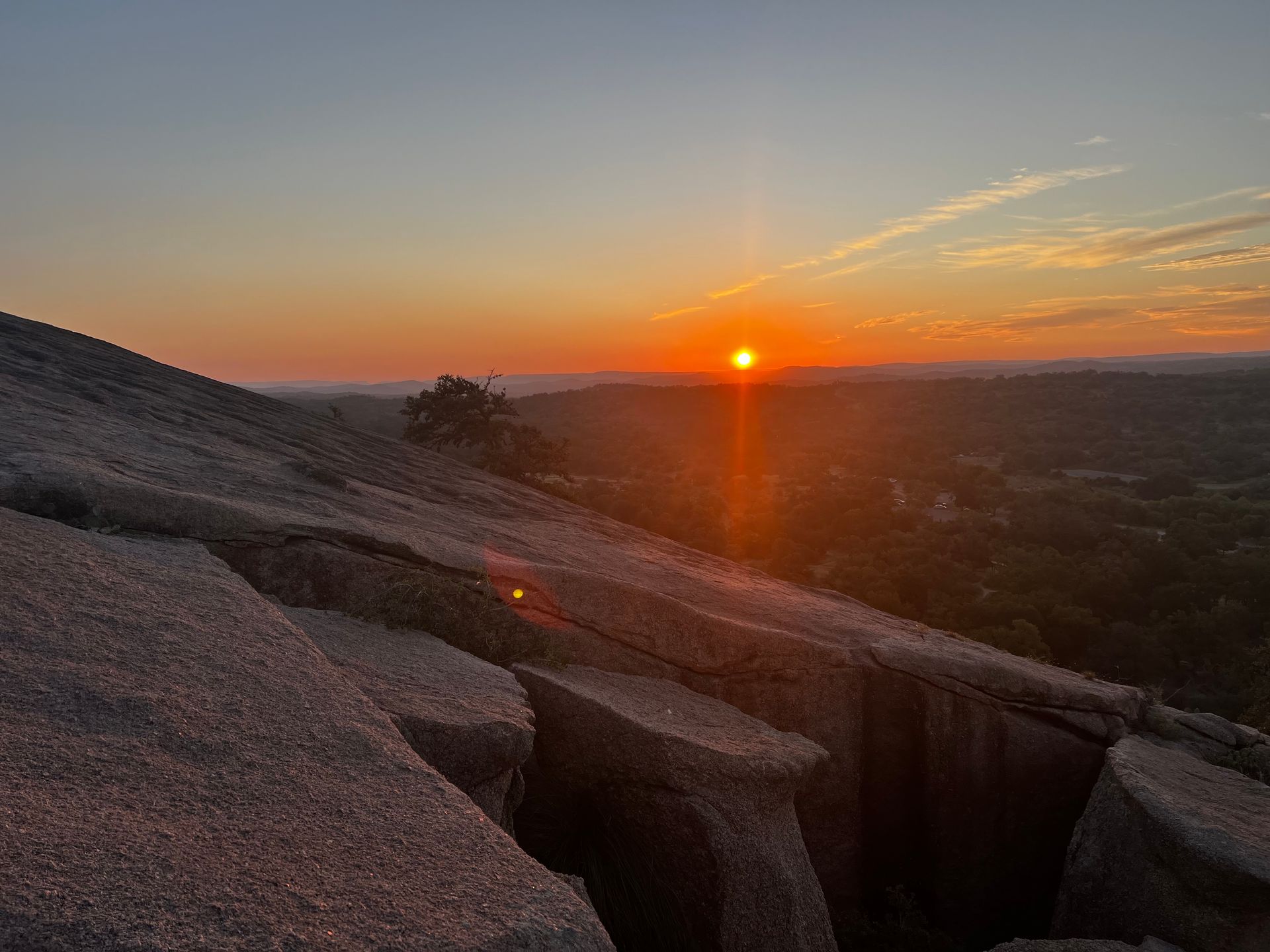 Water flows over a rock formation into a body of water, with green foliage in the background.