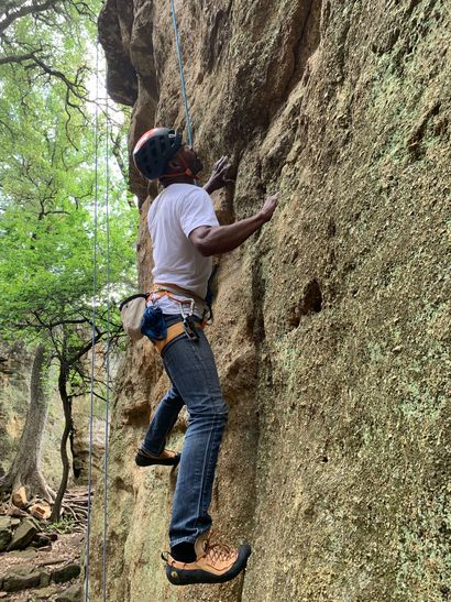 A man is climbing up a rock wall in the woods.