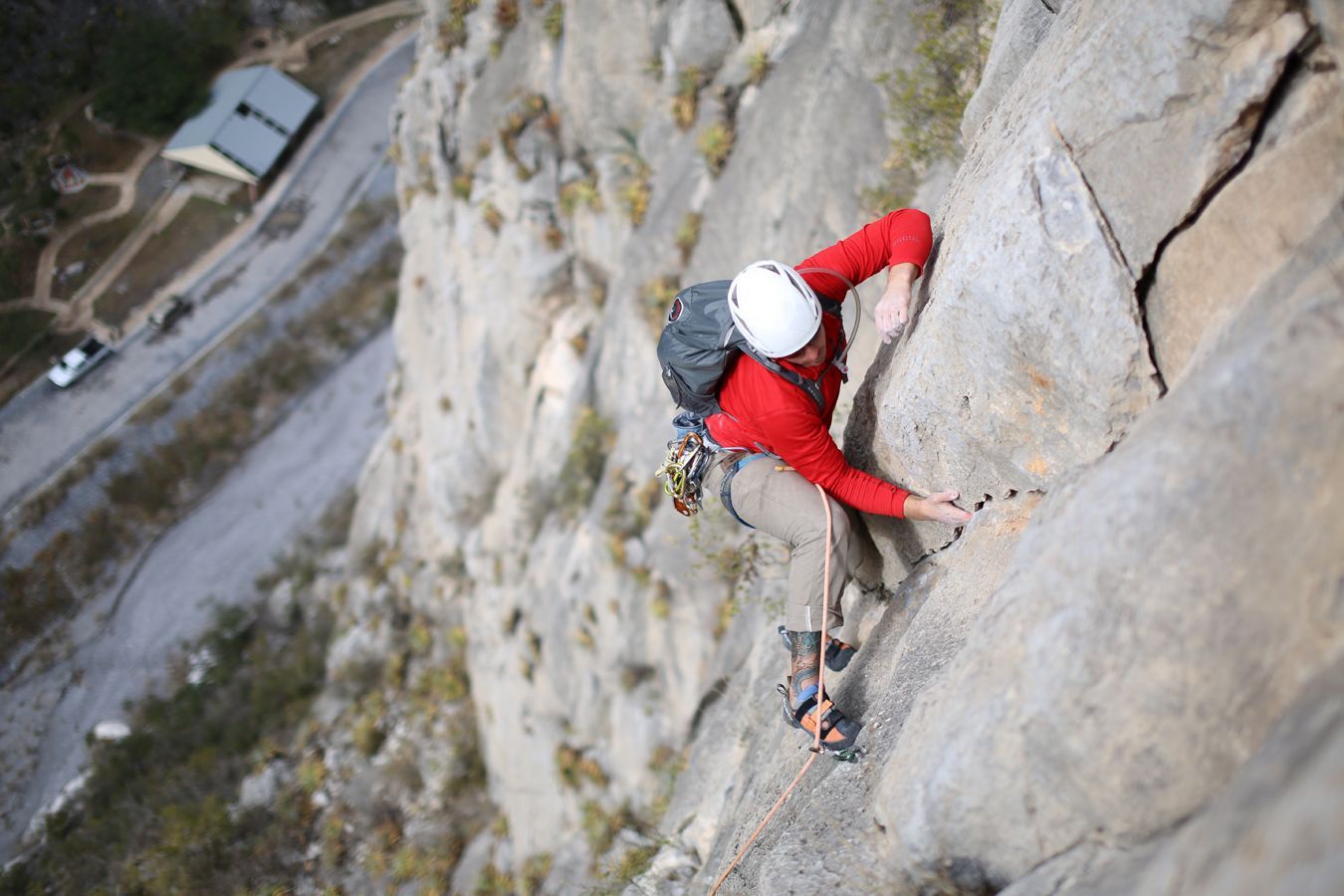 A man in a red shirt is climbing up a rock wall.