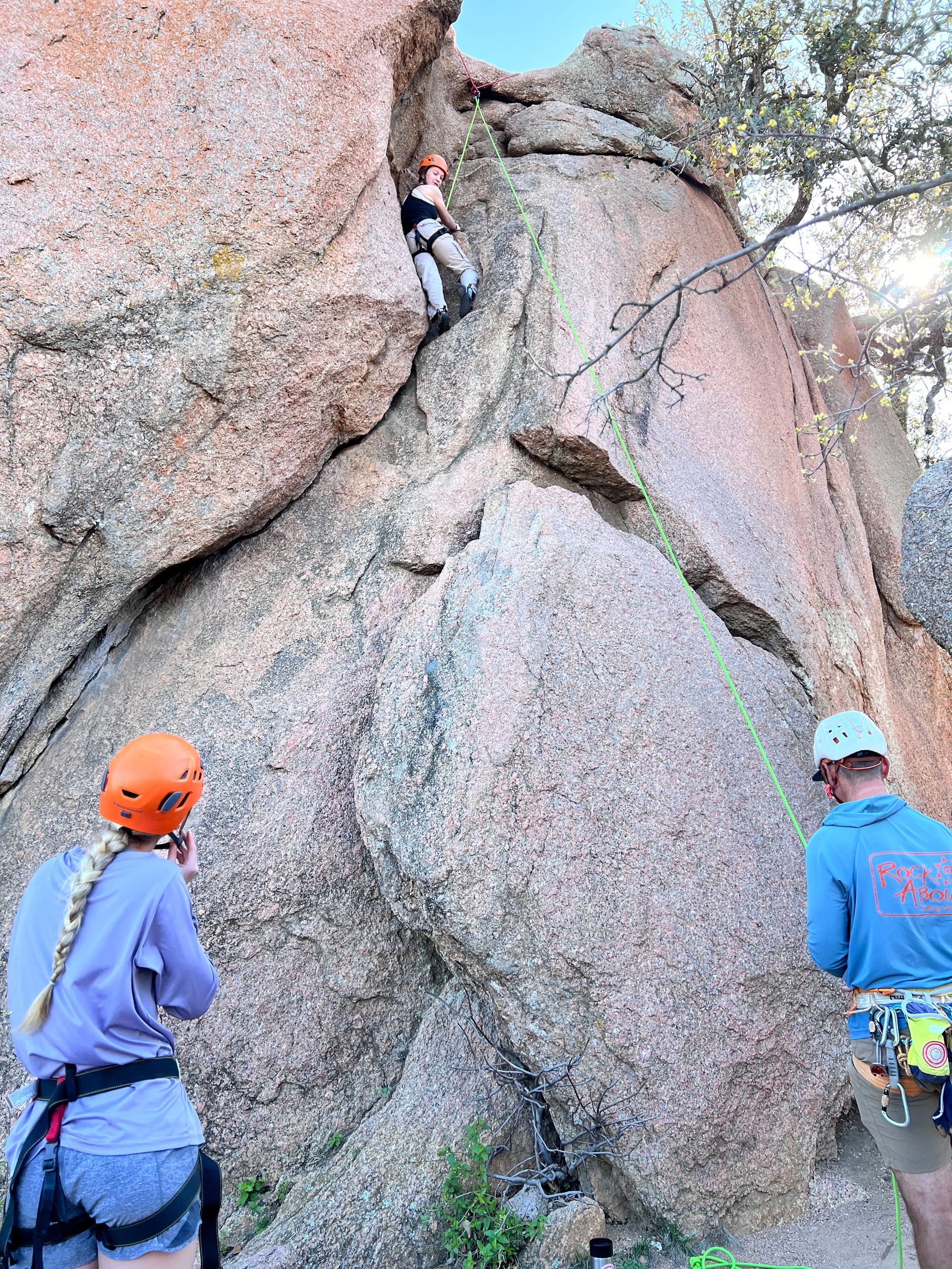 A child wearing an orange helmet climbs a rock