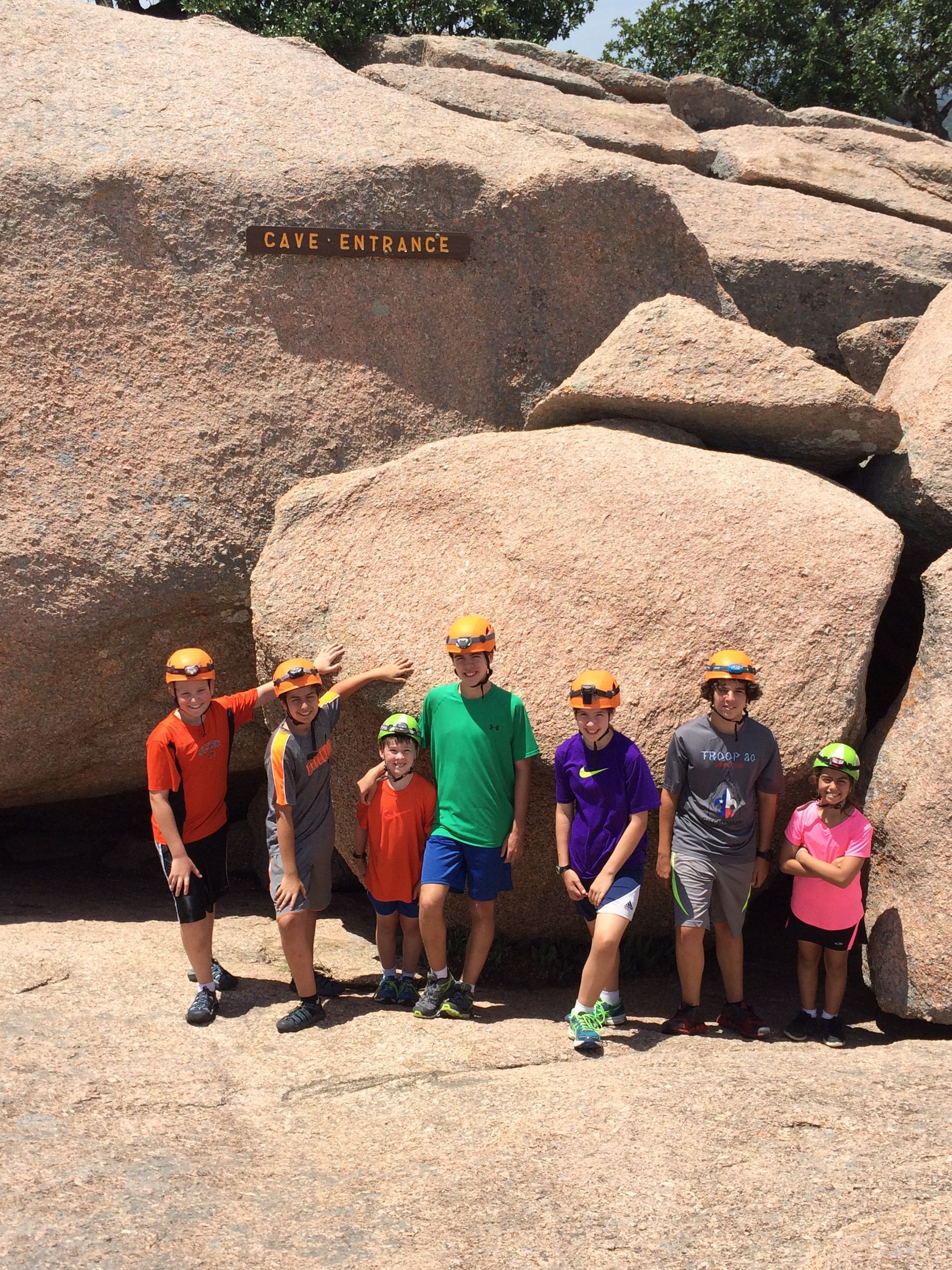 A group of children are posing for a picture in front of a large rock.