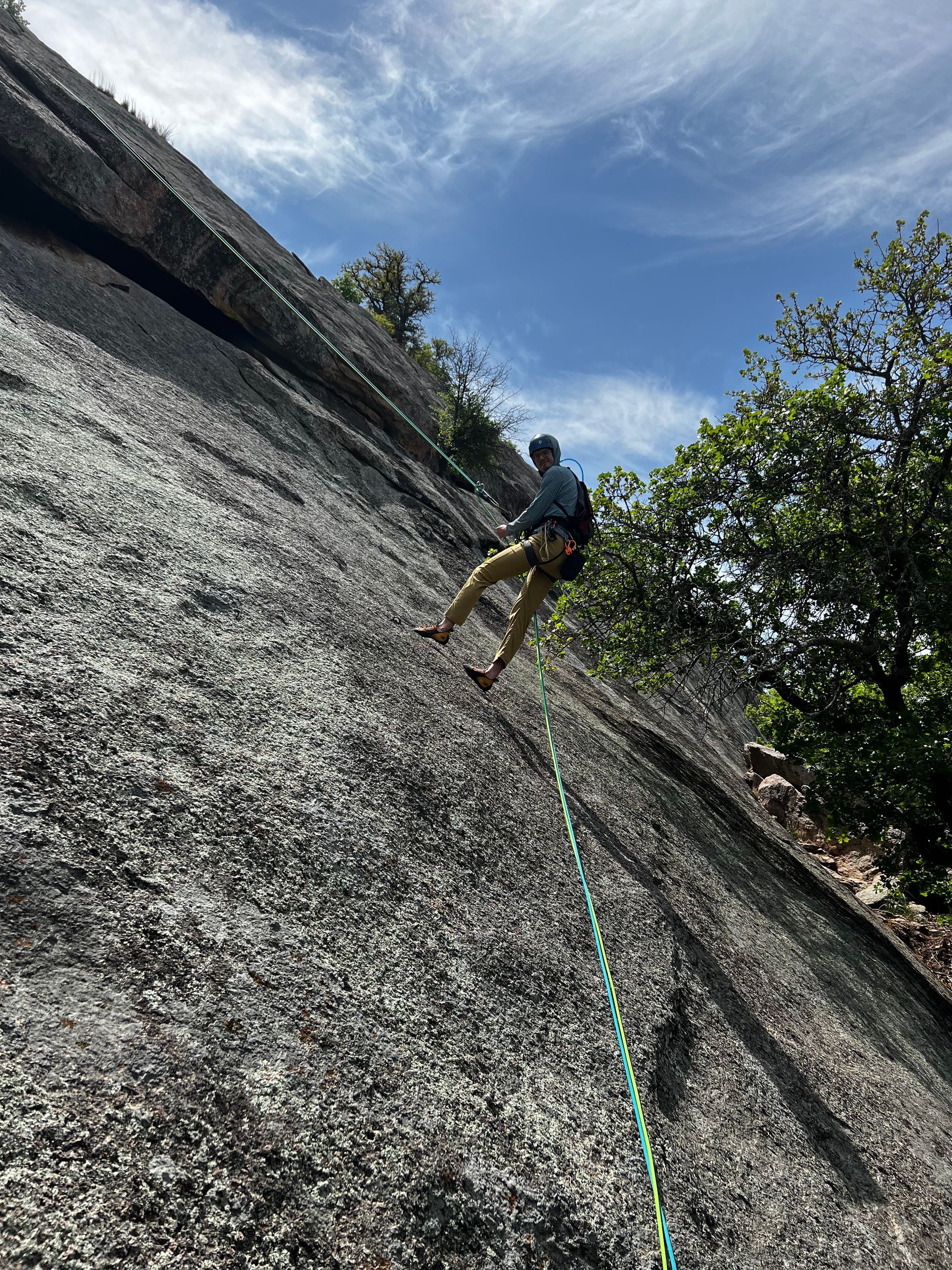 Woman rock climbing, wearing orange helmet, pink shirt, blue harness.