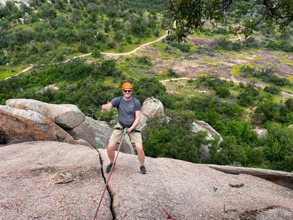 A man is standing on top of a rocky cliff holding a rope.