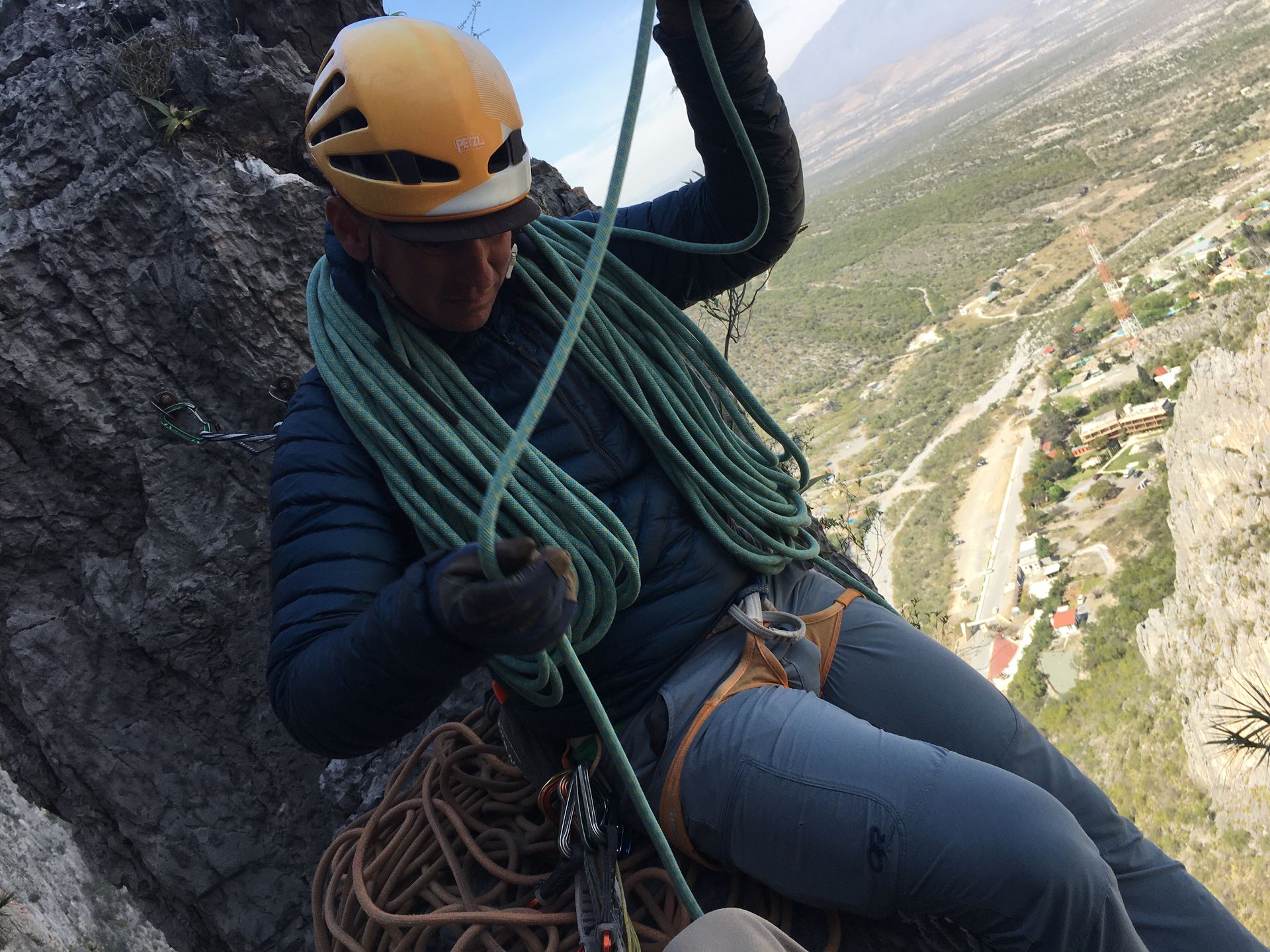 A man wearing a helmet is sitting on a rock holding a rope.