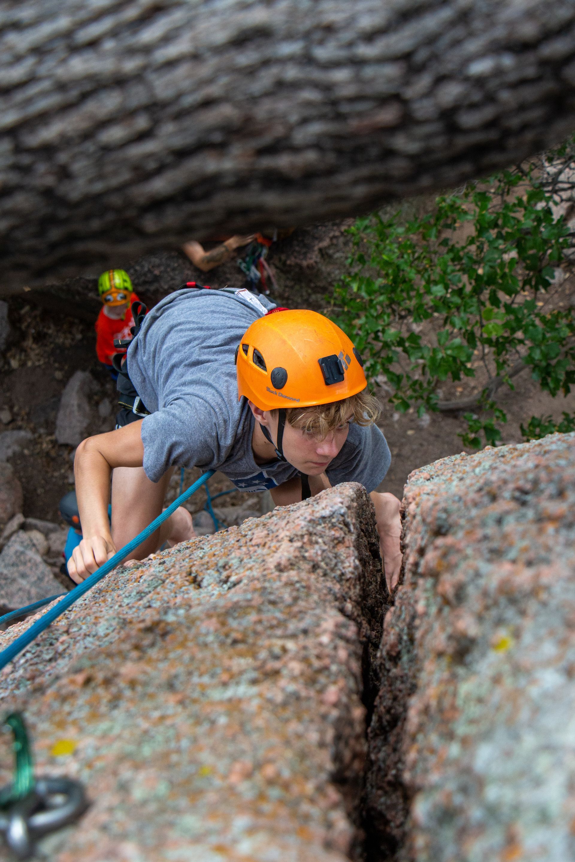 A child wearing an orange helmet climbs a rock