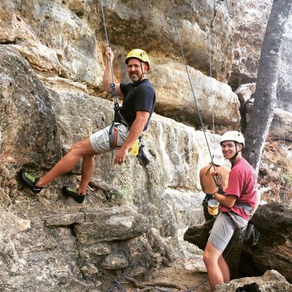 A man in a yellow helmet is climbing a rock wall