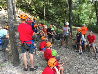 A group of people wearing helmets are sitting in a circle in the woods.