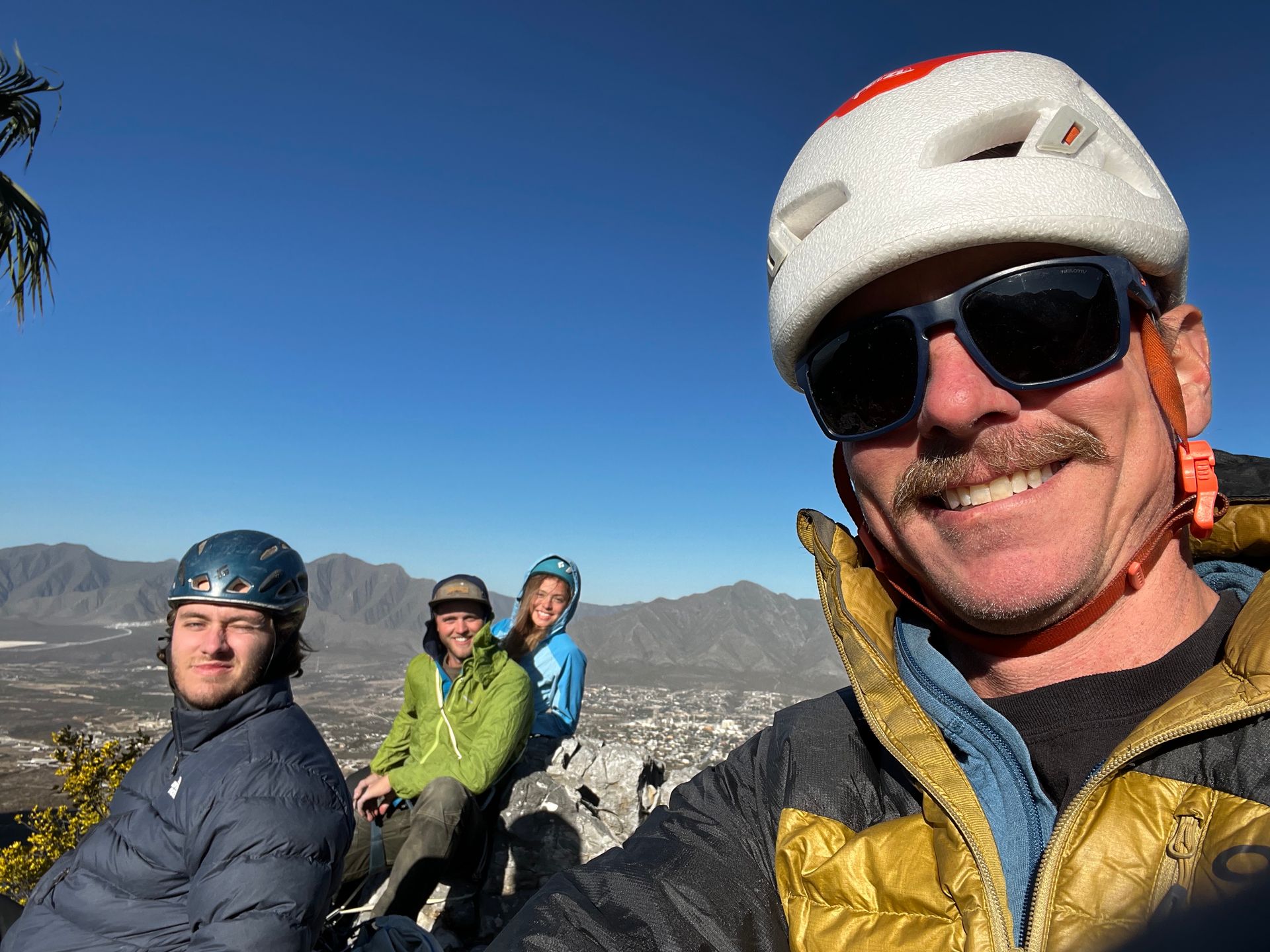 A man wearing a helmet and sunglasses is taking a selfie with two other people.