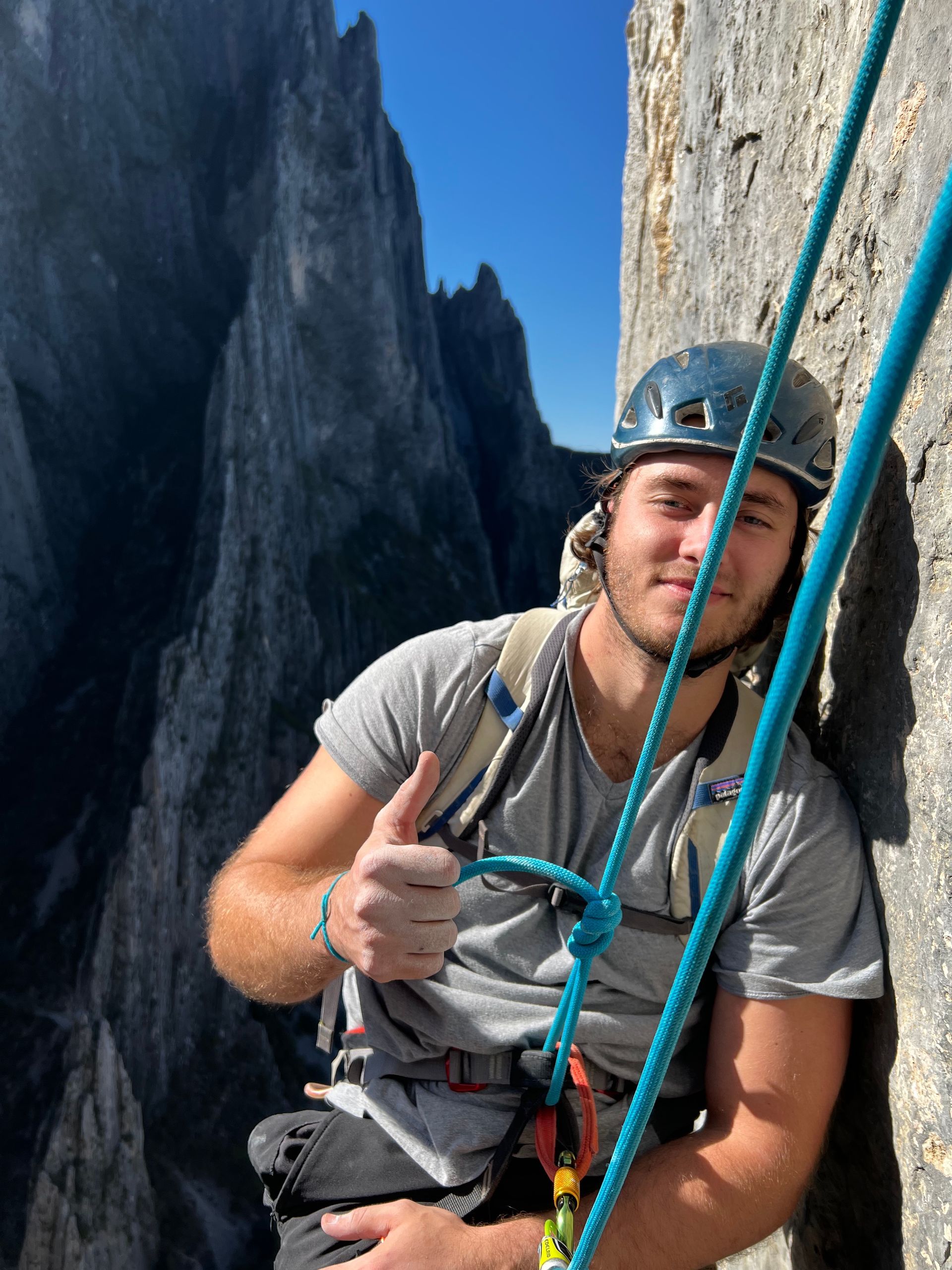 A man wearing a helmet is leaning against a rock and giving a thumbs up