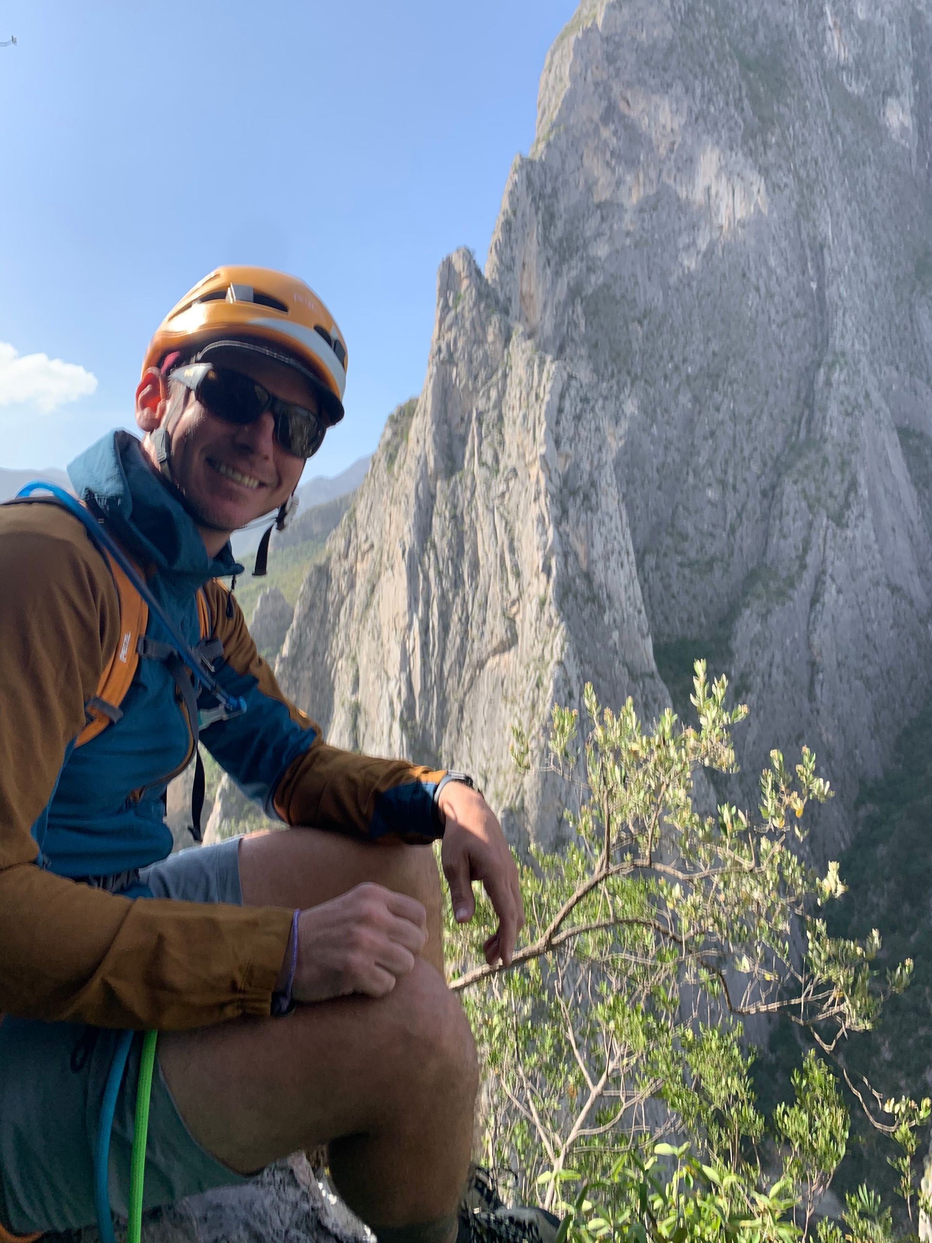 A man wearing a helmet and sunglasses is sitting on the edge of a mountain.