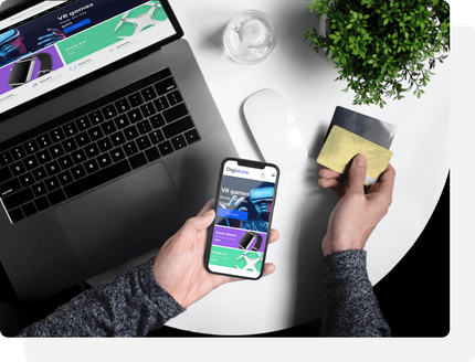 A person is holding a credit card and a cell phone in front of a laptop.